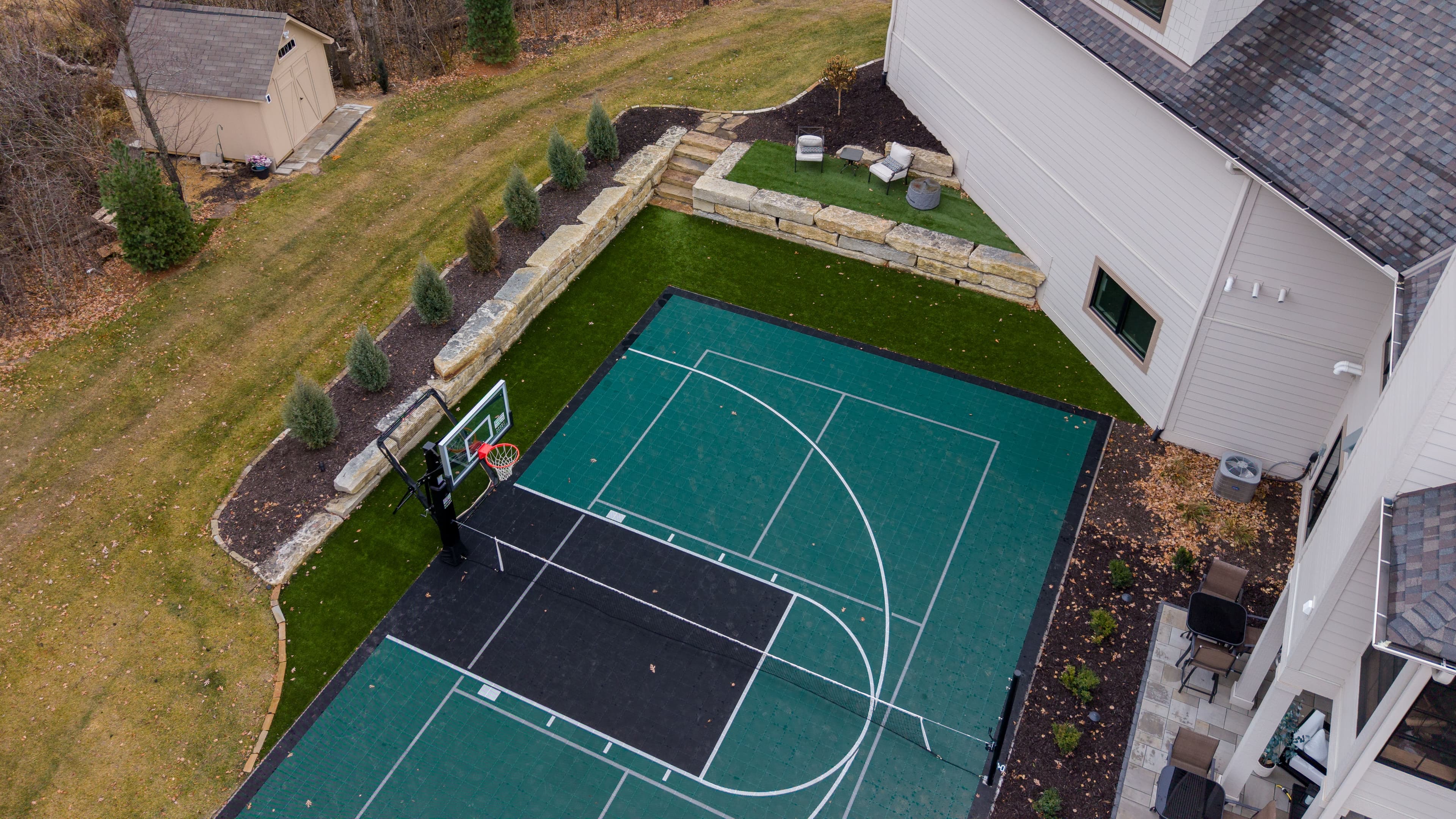 Aerial view of a backyard basketball court surrounded by landscaped features.