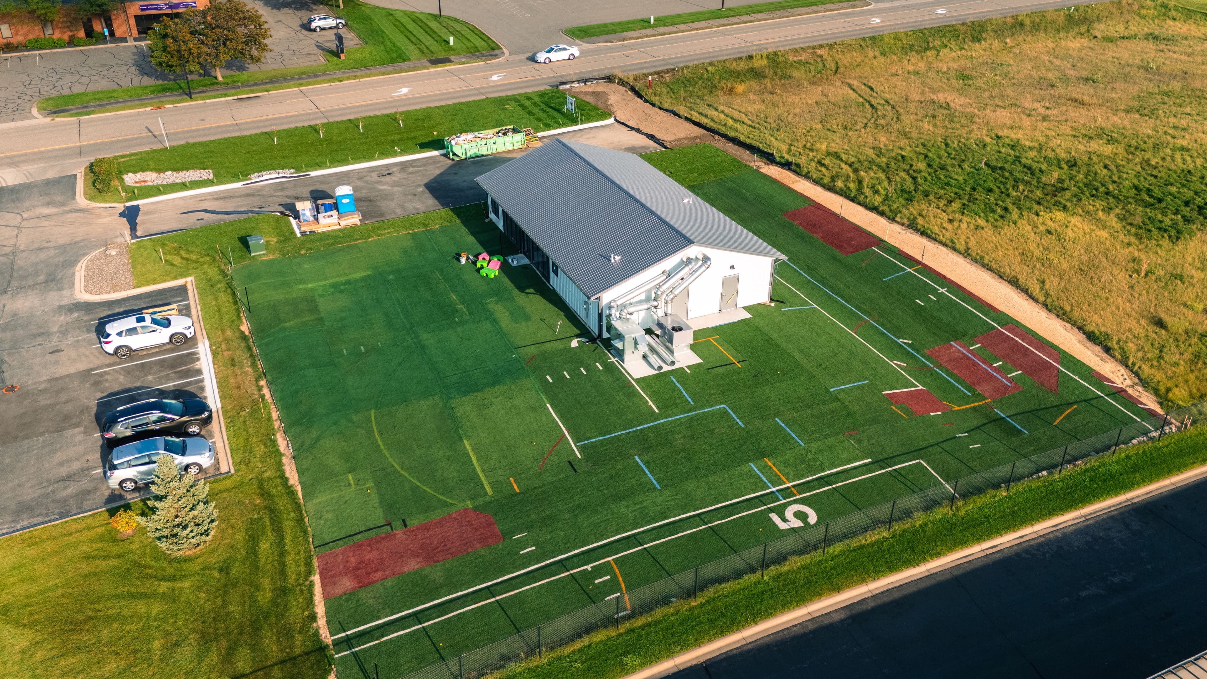 Aerial view of a sports training facility with artificial turf and parking area.