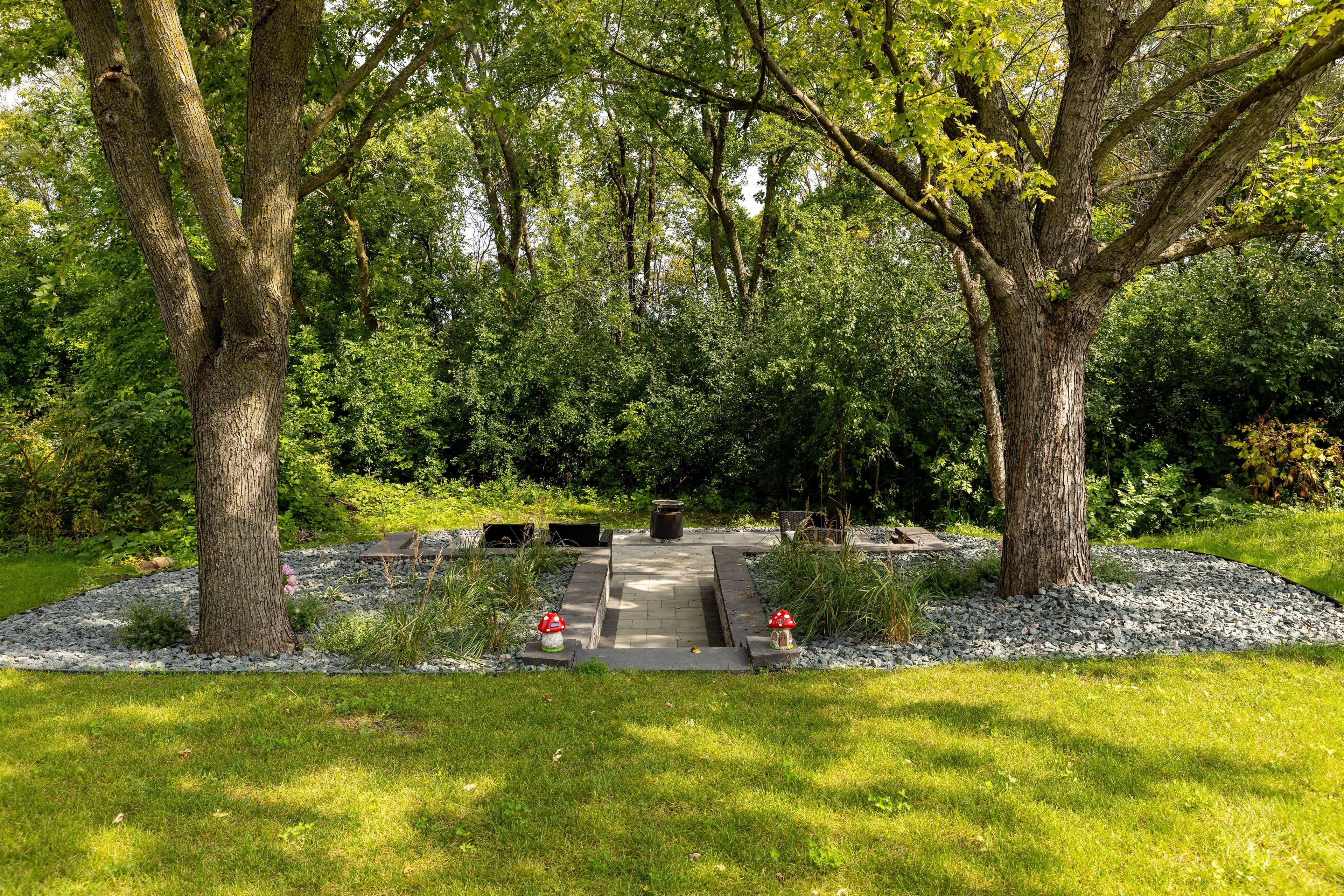 Serene outdoor garden with stone path, trees, and flowers surrounded by lush greenery.