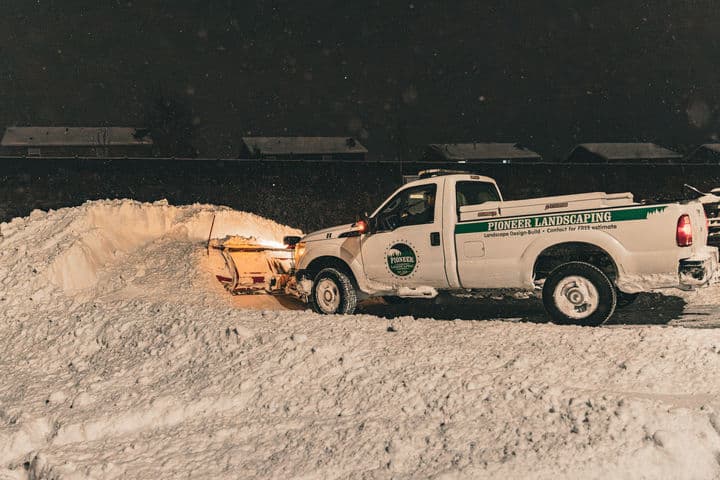 Pioneer Landscaping snowy truck clearing snow at night in a residential area.