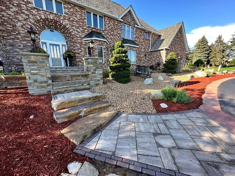 Brick house with landscaped garden, stone steps, and decorative shrubs and mulch.
