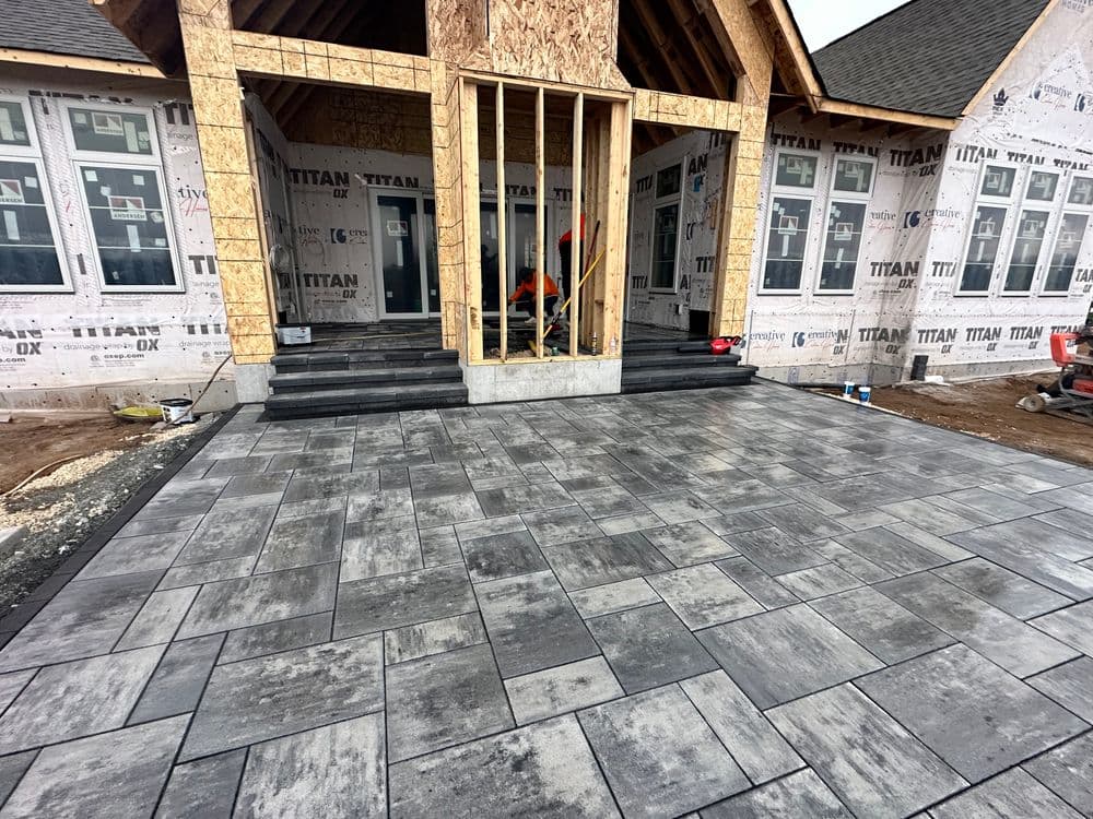 Newly installed gray paver patio in front of a house under construction.