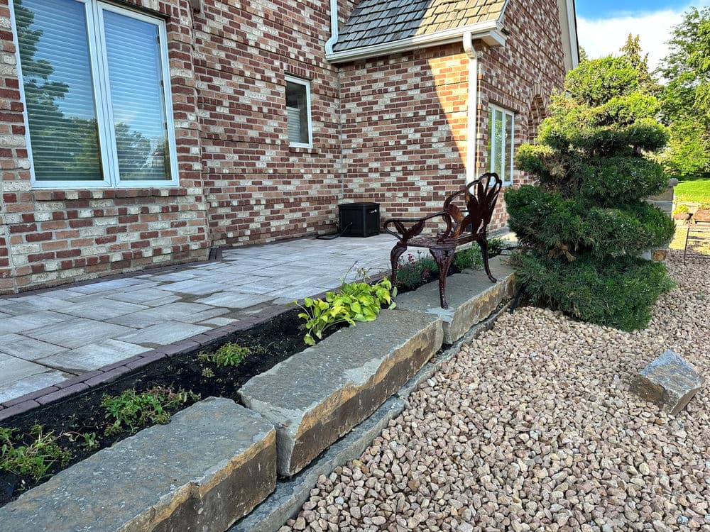 Patio area with brick house, ornamental bench, plants, and gravel landscaping.