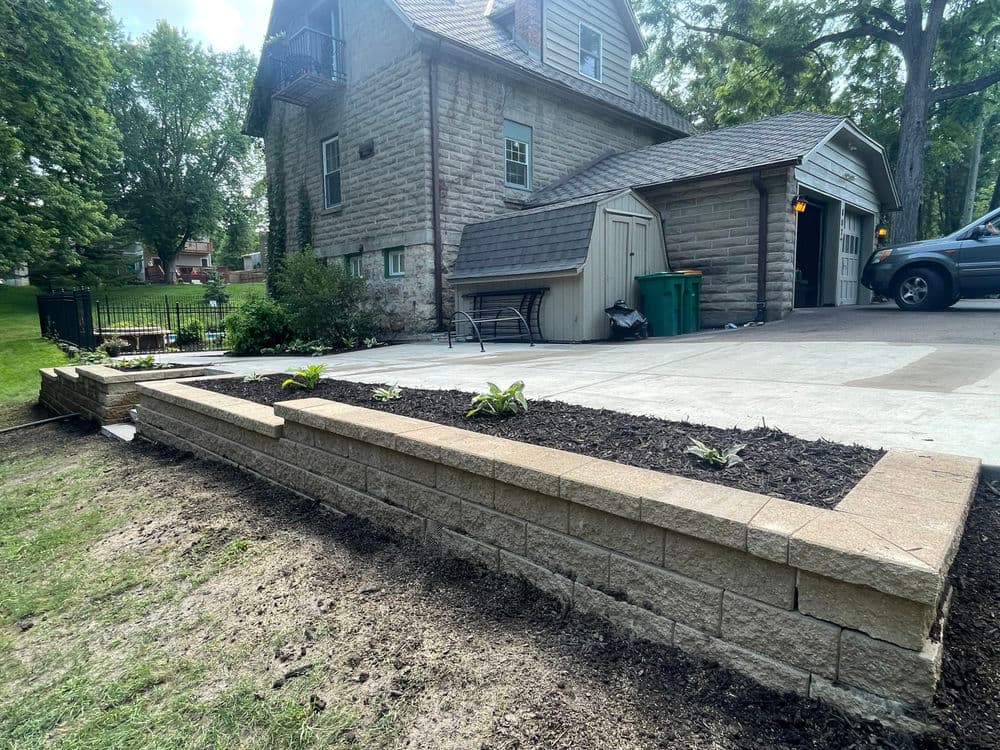 Stone retaining wall with planted beds near a residential home and driveway.