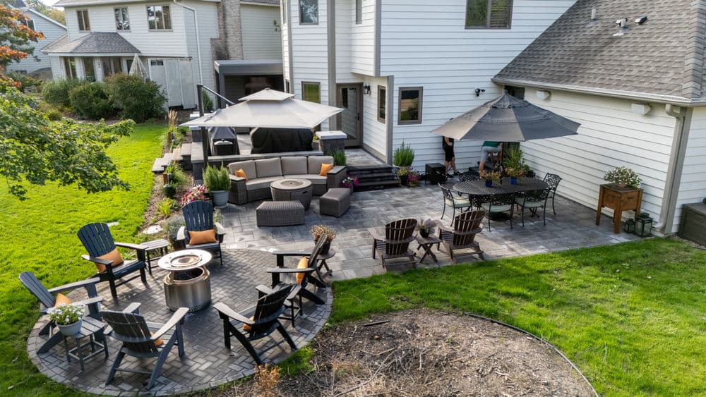 Backyard patio with seating, fire pit, and dining area surrounded by lush greenery.