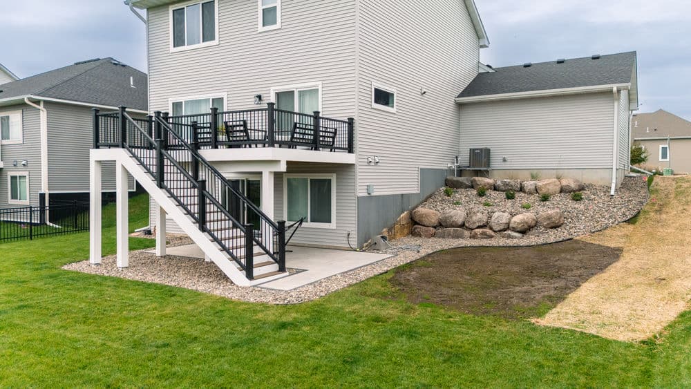 Modern home exterior featuring a two-level deck, landscaped yard, and rocky garden area.