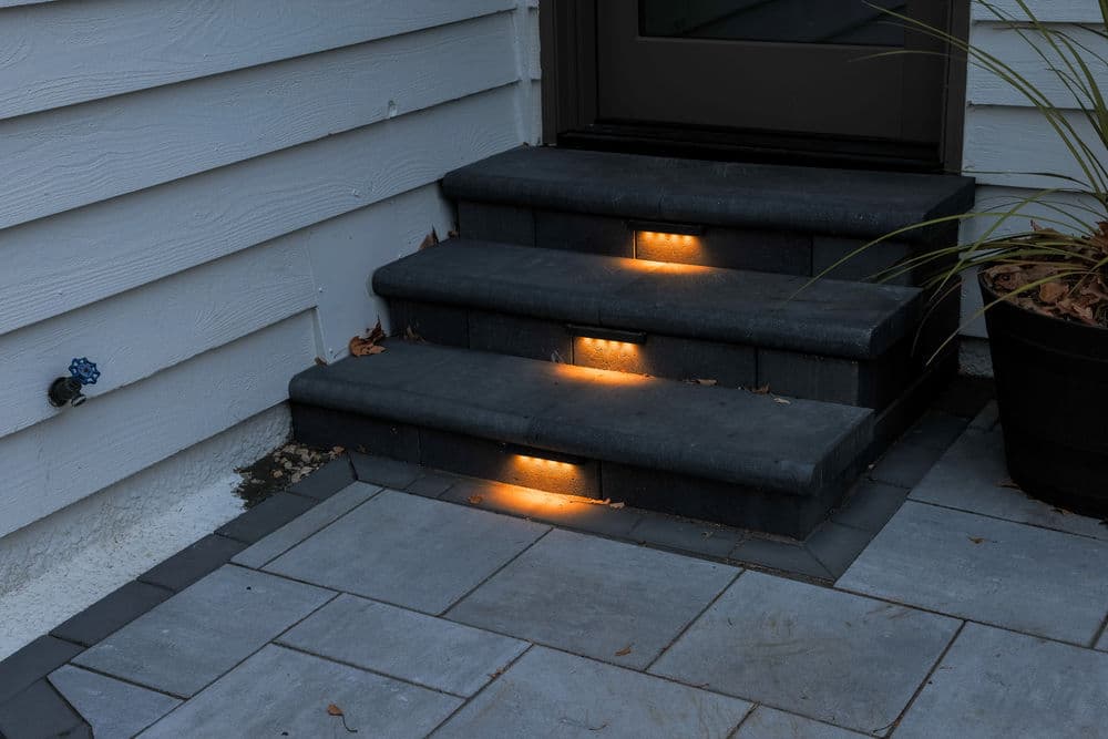 Illuminated outdoor stone steps leading to a door, featuring recessed lighting for safety.