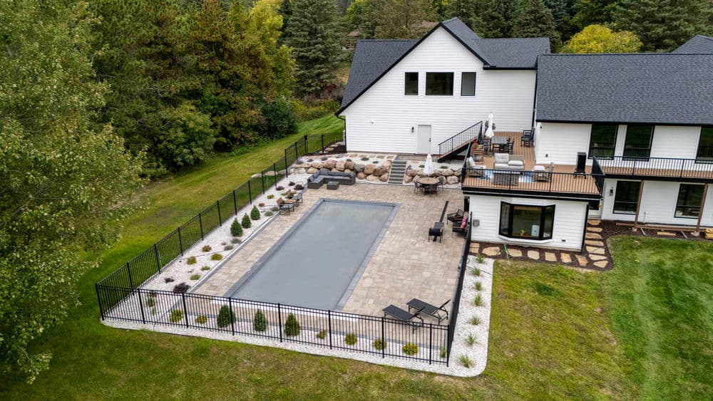 Aerial view of a modern home with a fenced pool, patio, and landscaped yard.