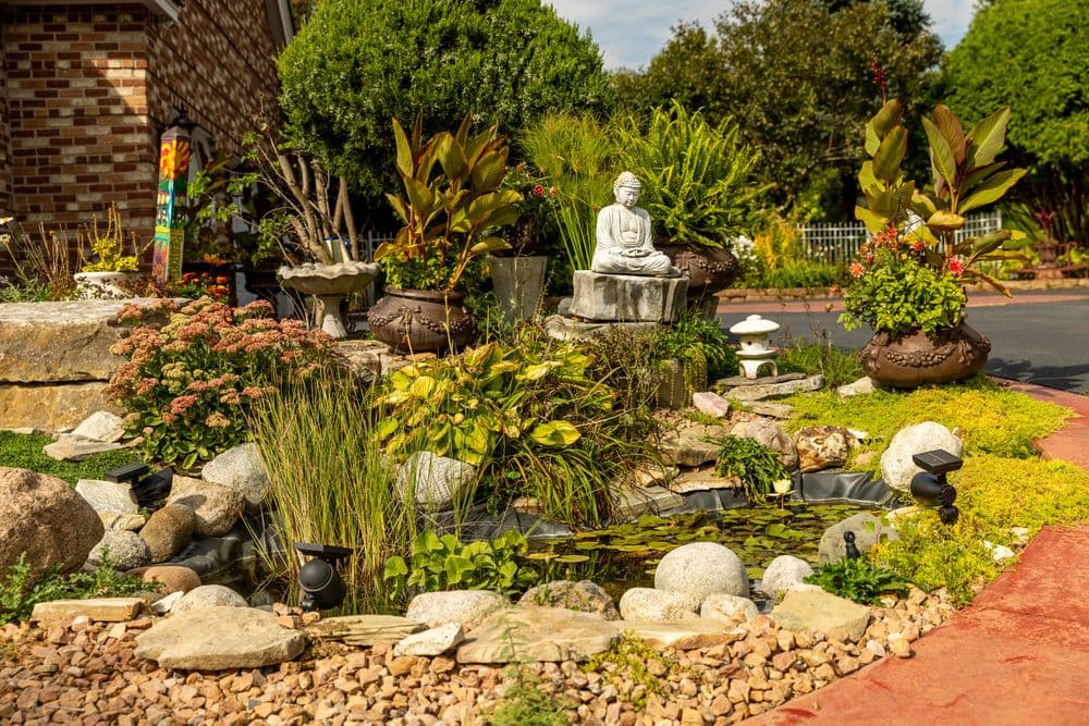 Beautiful garden landscape featuring a Buddha statue, lush plants, and a serene pond.