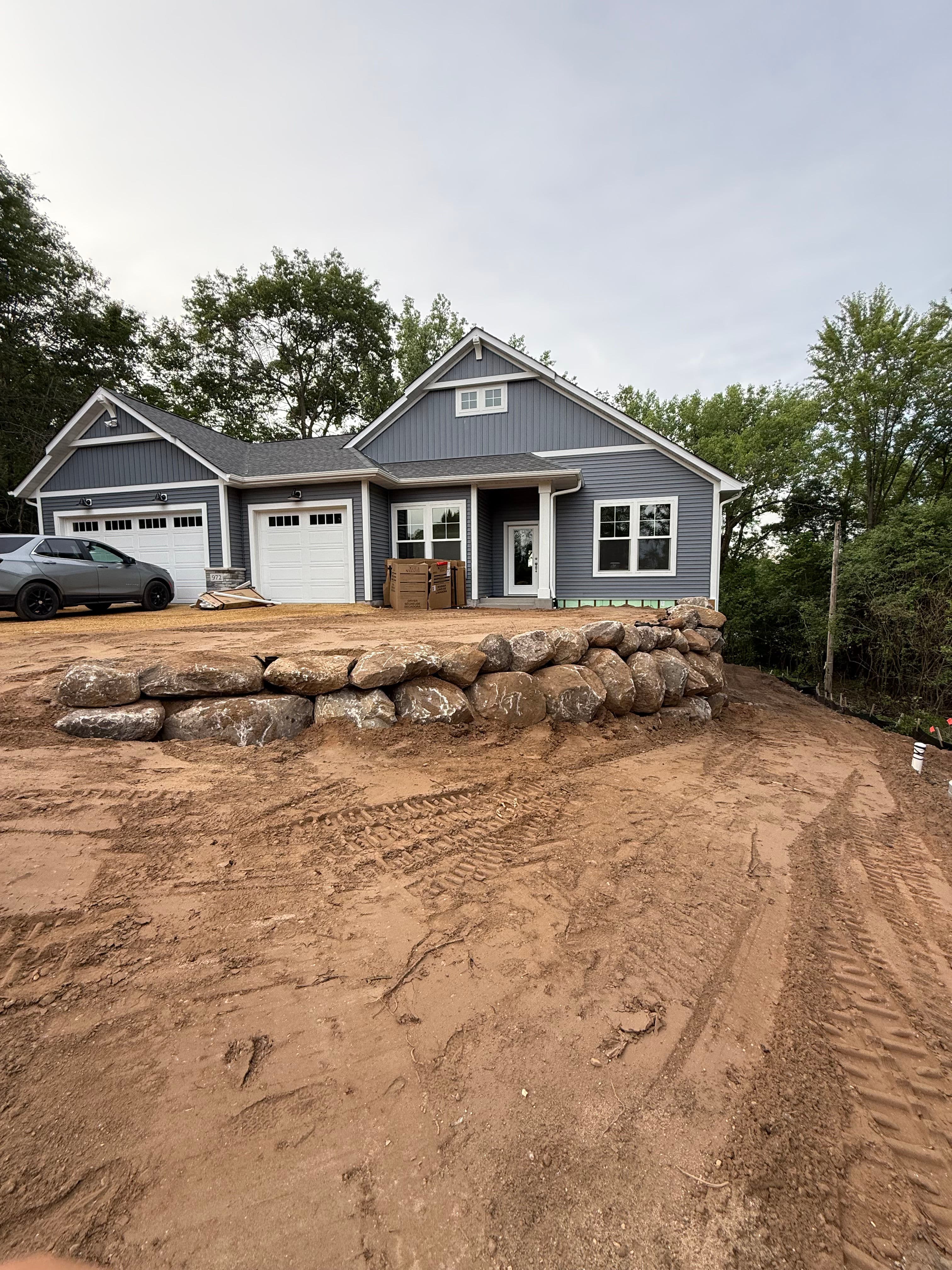 Newly constructed blue house with garage, stone landscaping, and natural surroundings.