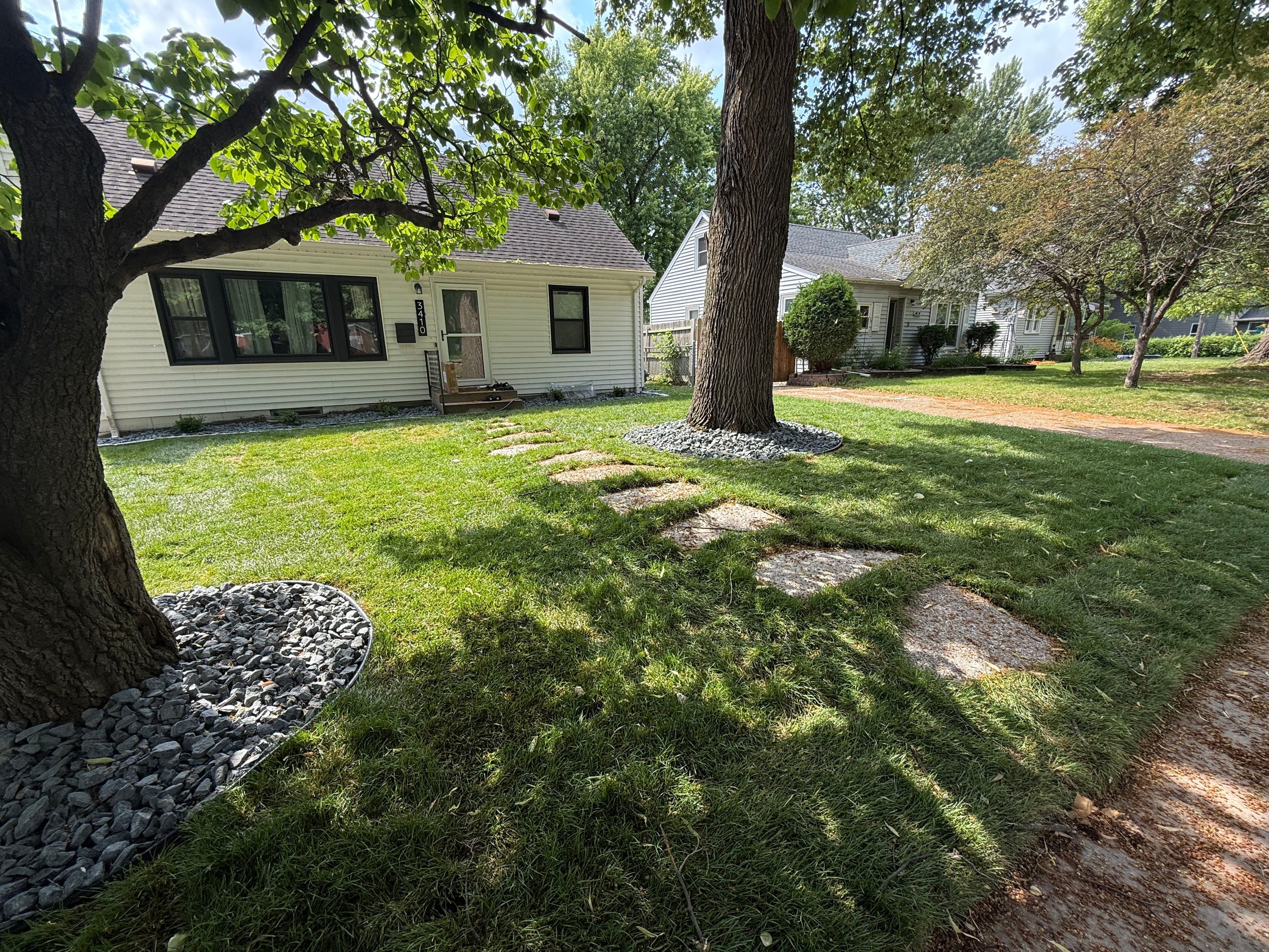 Lush green lawn with stepping stones and trees in a residential front yard.