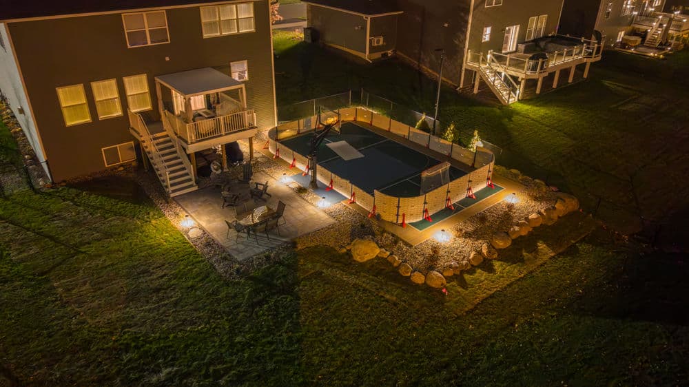 Aerial view of a well-lit backyard with a fenced sports court and seating area.