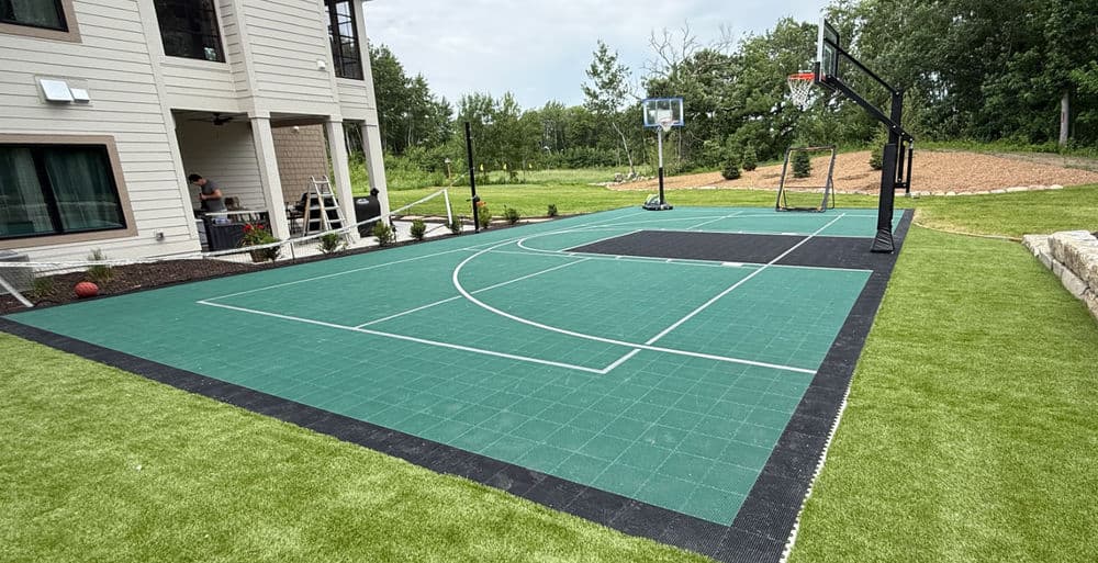 Backyard basketball court with green surface, hoop, and nearby landscaping. Perfect for sports enthusiasts.